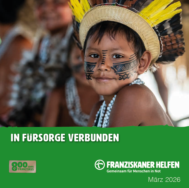 Ein indigenes Kind mit bemaltem Gesicht und traditionellem Federschmuck blickt in die Kamera. Es trägt eine Kette aus Perlen; im Hintergrund sind weitere Personen unscharf zu erkennen.