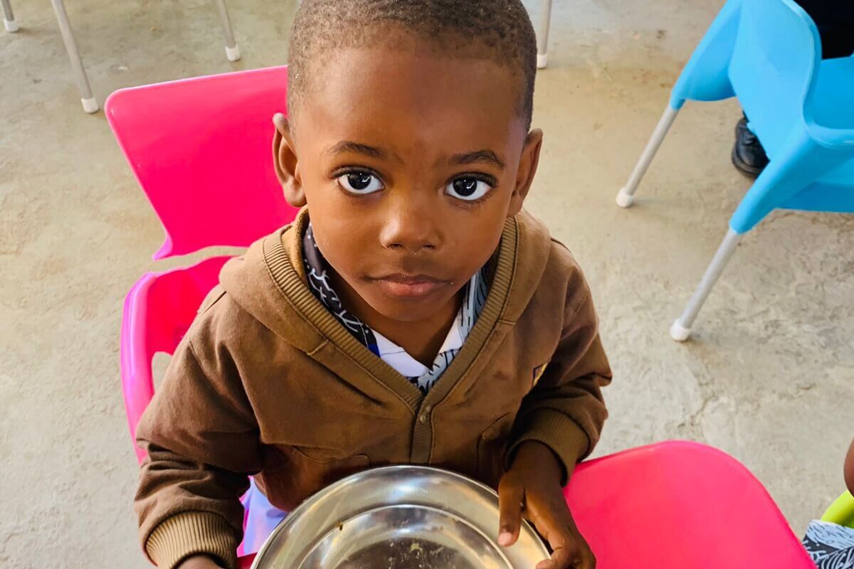 Kind sitzt mit leerem Teller in einer Betreuungseinrichtung. Franziskaner Helfen unterstützt Kinder und Familien mit Nahrungsmitteln und hilft gegen Hunger und Unterernährung.