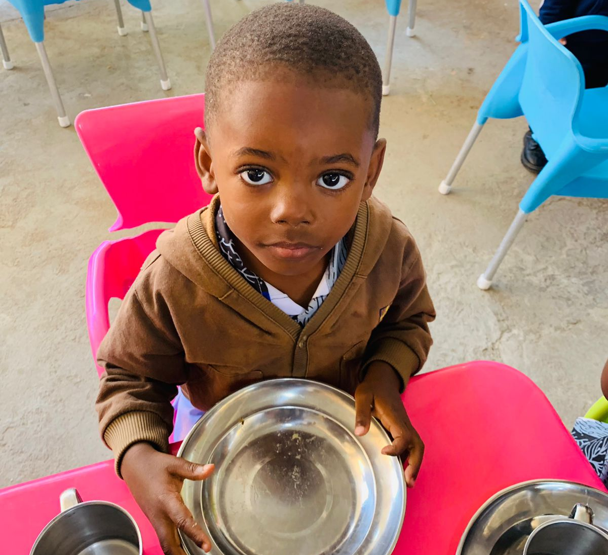 Kind sitzt mit leerem Teller in einer Betreuungseinrichtung. Franziskaner Helfen unterstützt Kinder und Familien mit Nahrungsmitteln und hilft gegen Hunger und Unterernährung.