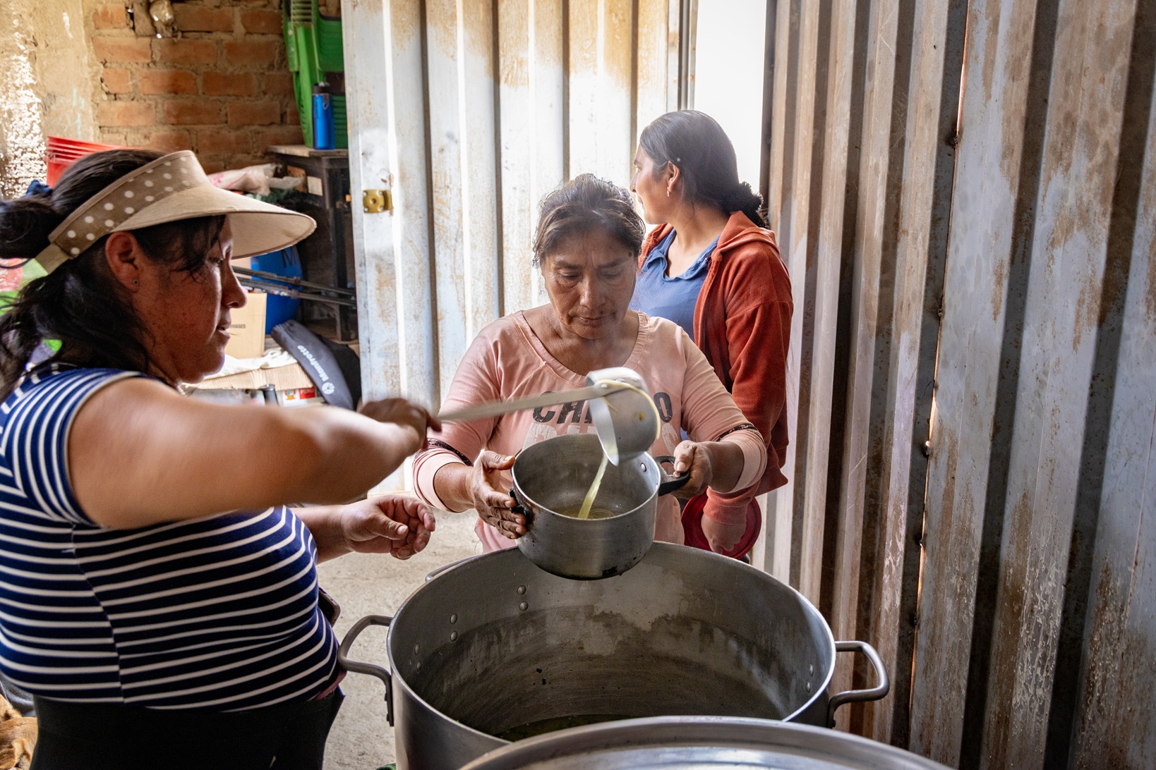 Frauen schöpfen Essen aus einem großen Kochtopf in einer Suppenküche von Franziskaner Helfen in Huaycán, Peru.