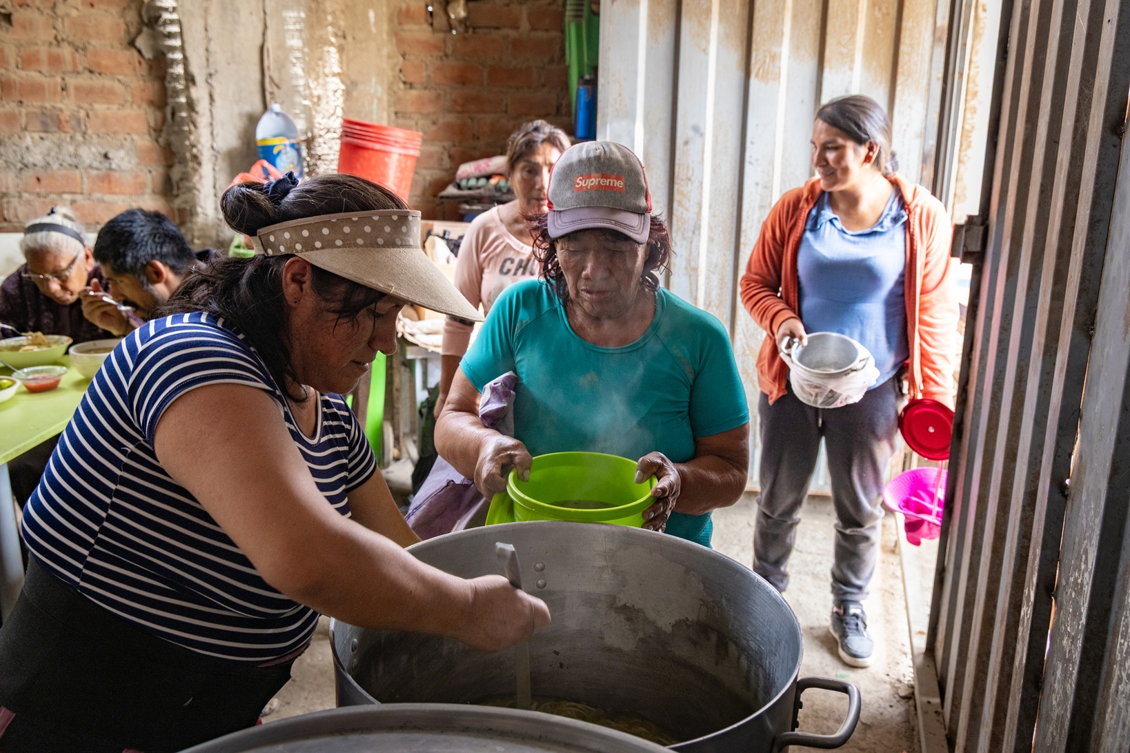 rauen schöpfen Essen aus einem großen Kochtopf in einer Suppenküche von Franziskaner Helfen in Huaycán, Peru.