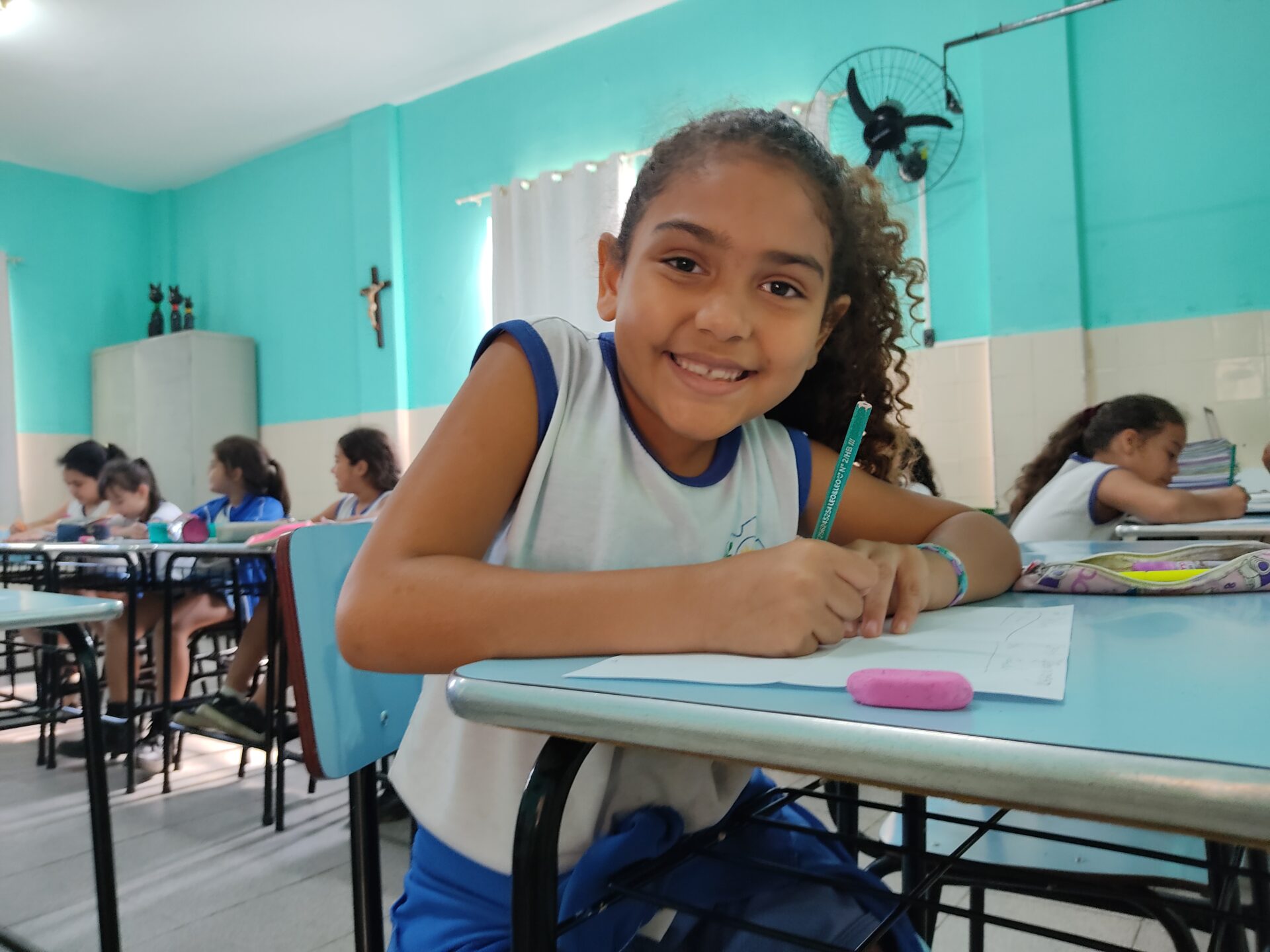 Lächelndes Schulmädchen beim Lernen im Klassenzimmer gemeinsam mit anderen Kindern.