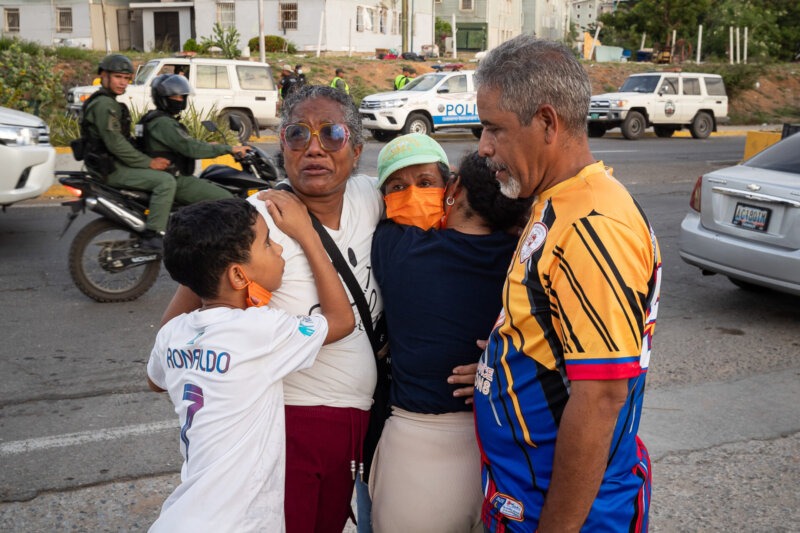 Familie umarmt sich nach dem Erdbeben in Venezuela auf der Straße, während Einsatzkräfte im Hintergrund im Einsatz sind.