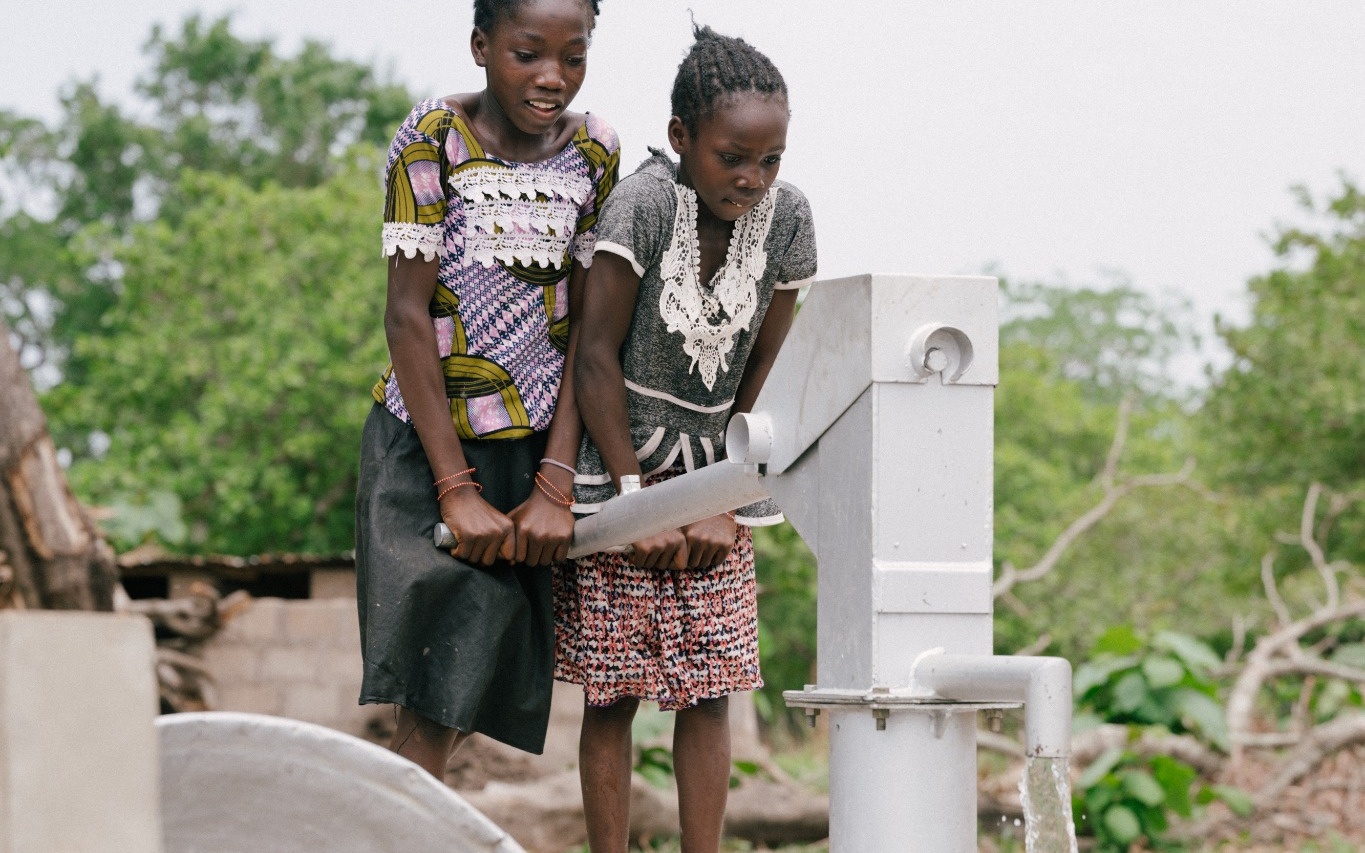 Zwei Mädchen pumpen Wasser an einem Handpumpenbrunnen in einem Projekt von Franziskaner Helfen.