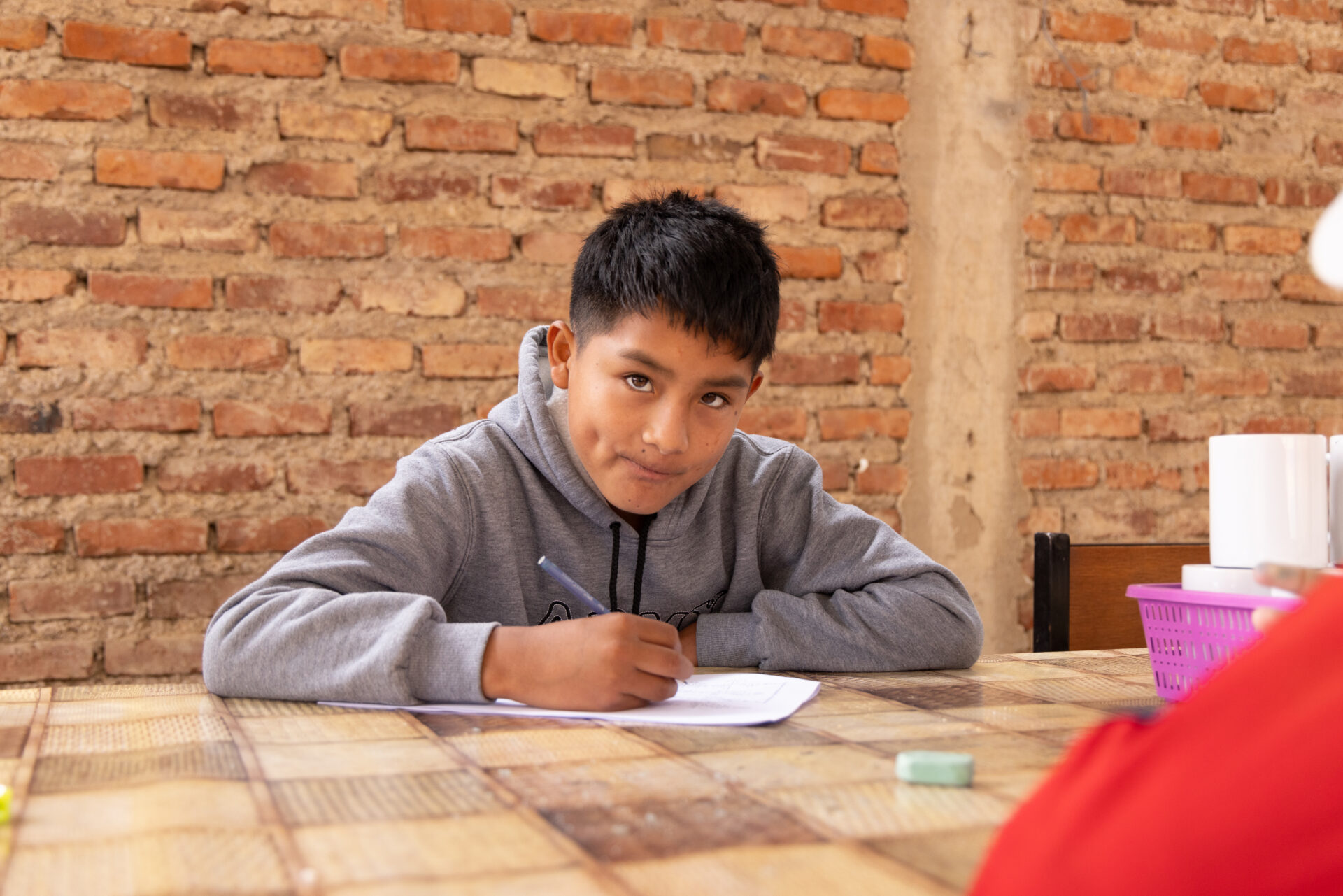 Jhonatan sitzt am Tisch und schreibt in ein Schulheft in einer Tagesstätte in Bolivien.